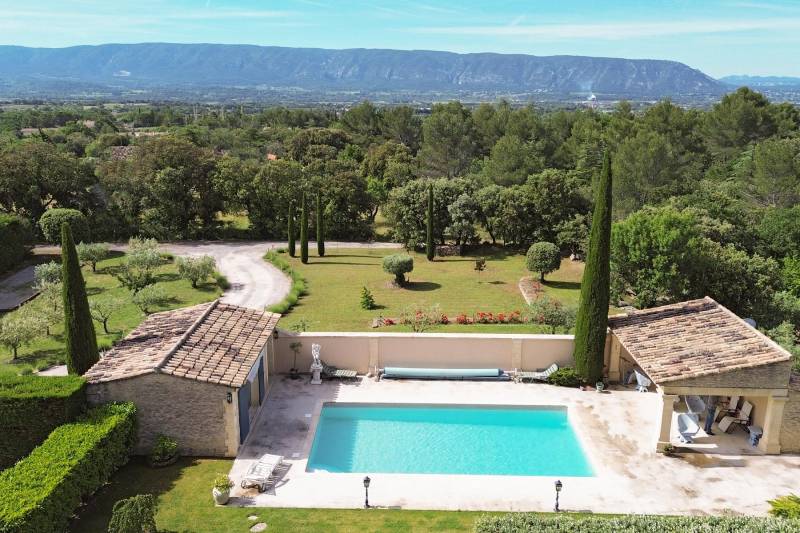 Entre Gordes et Cabrières d'Avignon, face au Luberon et ses villages perchés, propriété en pierres avec piscine chauffée, pool house et dépendances à vendre en Provence.