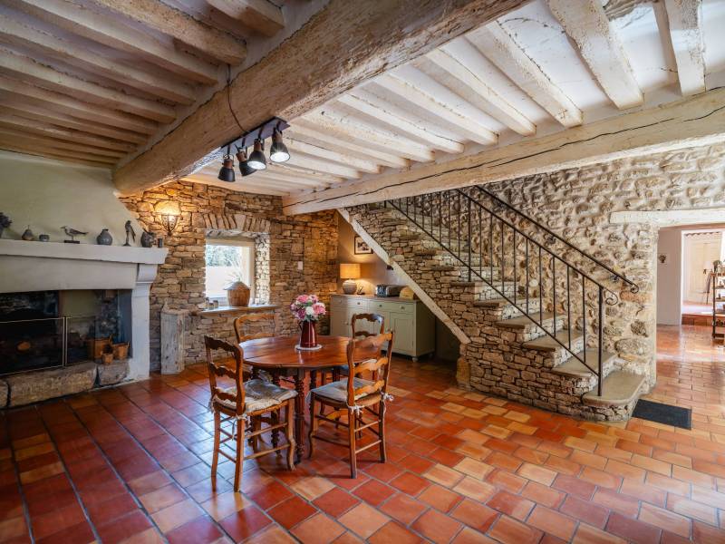 Authenticité préservée : Salle à manger de caractère mettant en valeur les pierres apparentes, le sol en terre cuite et un escalier artisanal.